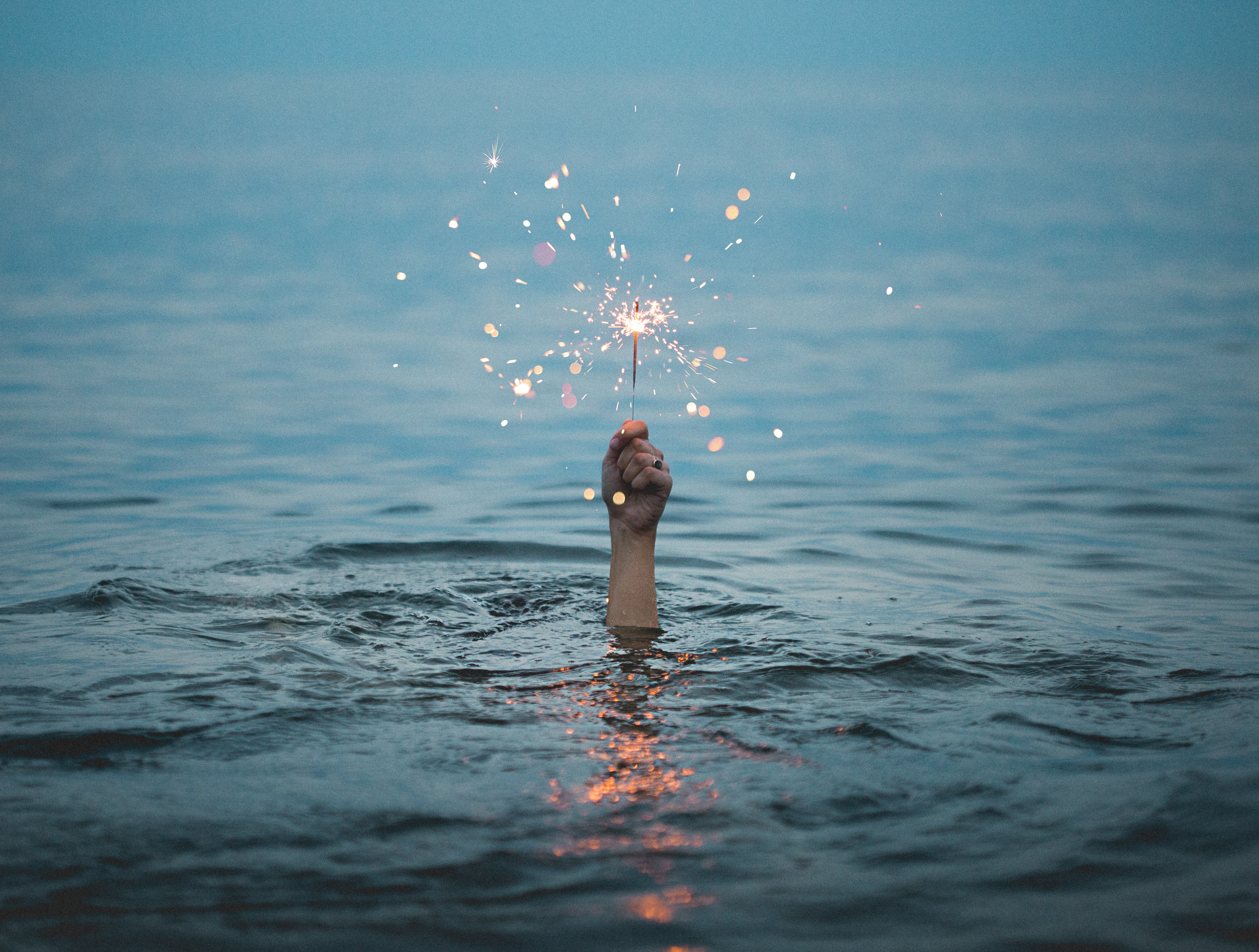 person submerged in water holding a sparkler