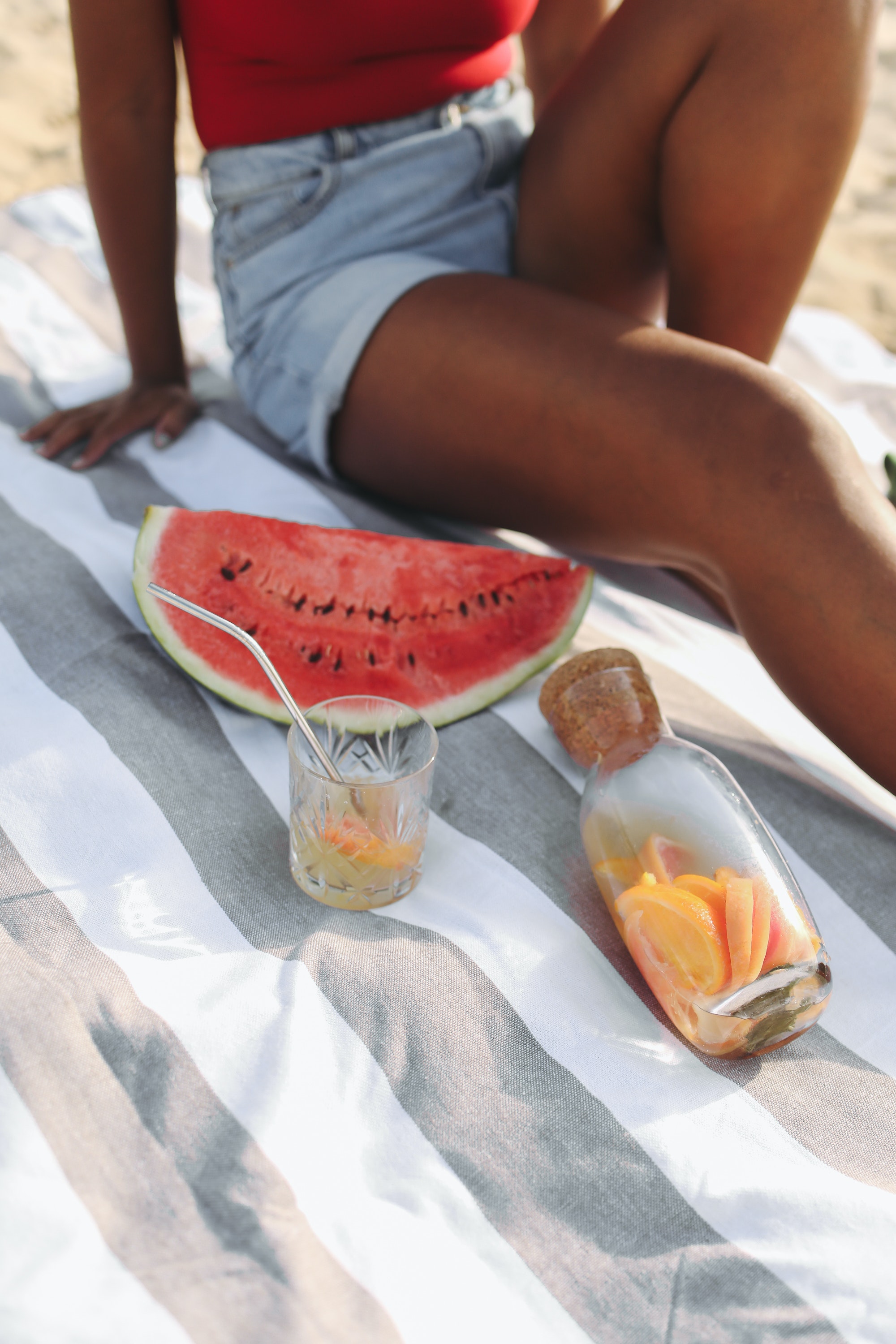 woman sitting on a blanket at the beach with water and fruit